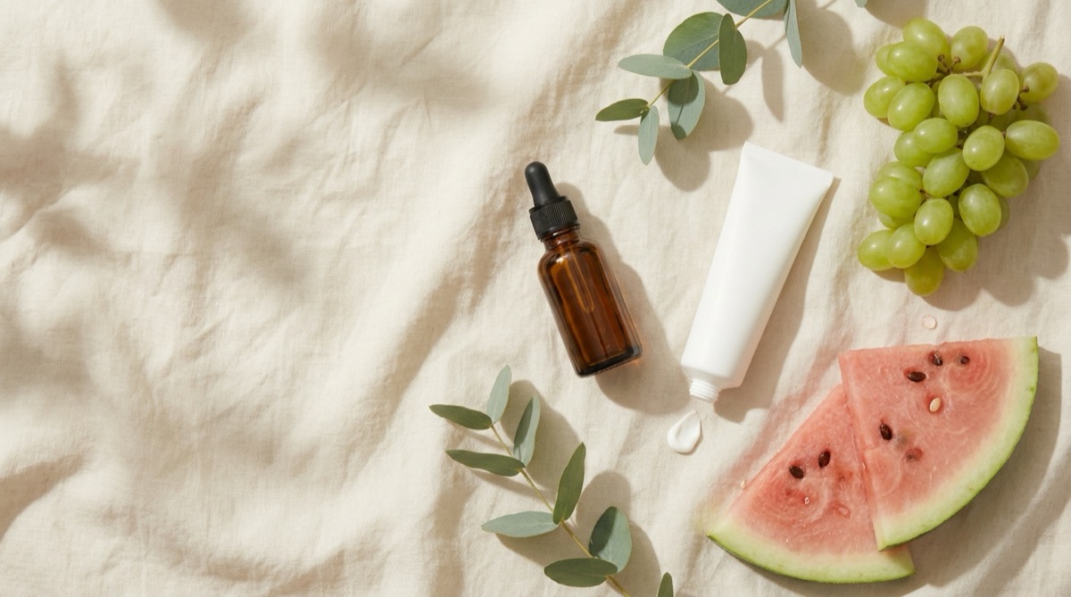 Dropper bottle, moisturizer, and summer fruit on natural linen.